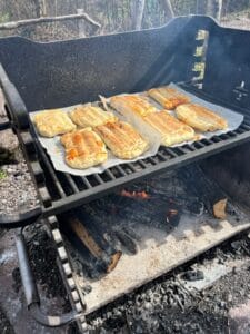 Das Bild zeigt einen Holzkohlegrill, auf dem gerade selbstgemachte Calzone-Pizzen gebacken werden.